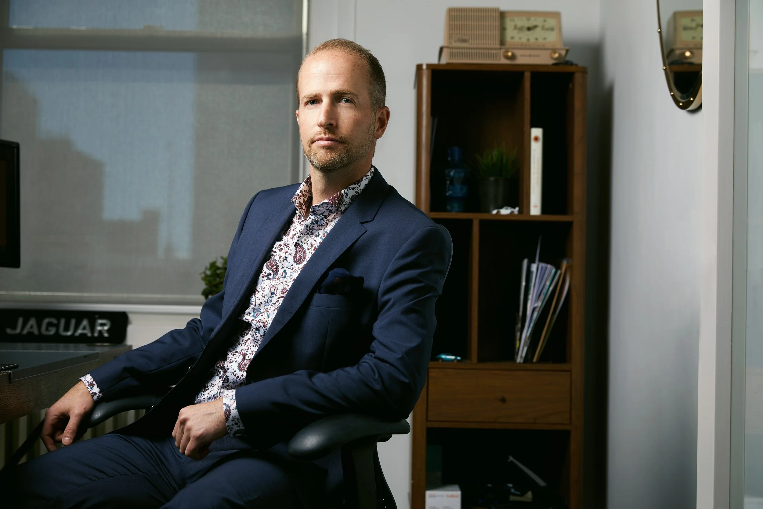 Office portrait in a desk chair, navy suit and floral shirt