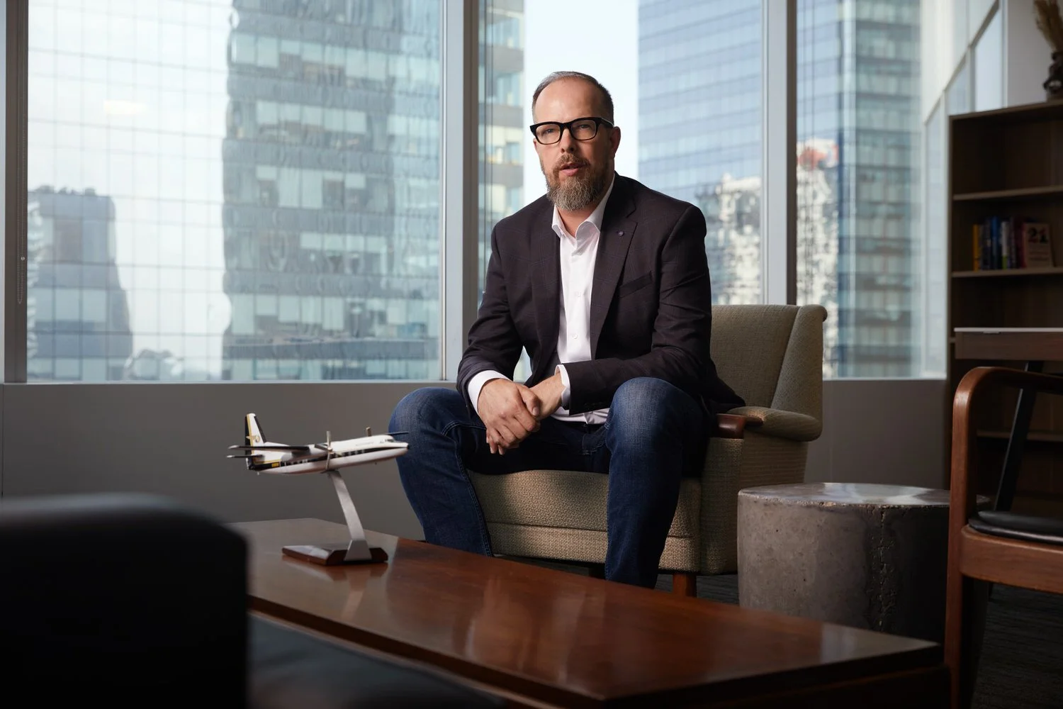 Office portrait seated by the window, towers behind, a model plane on the table