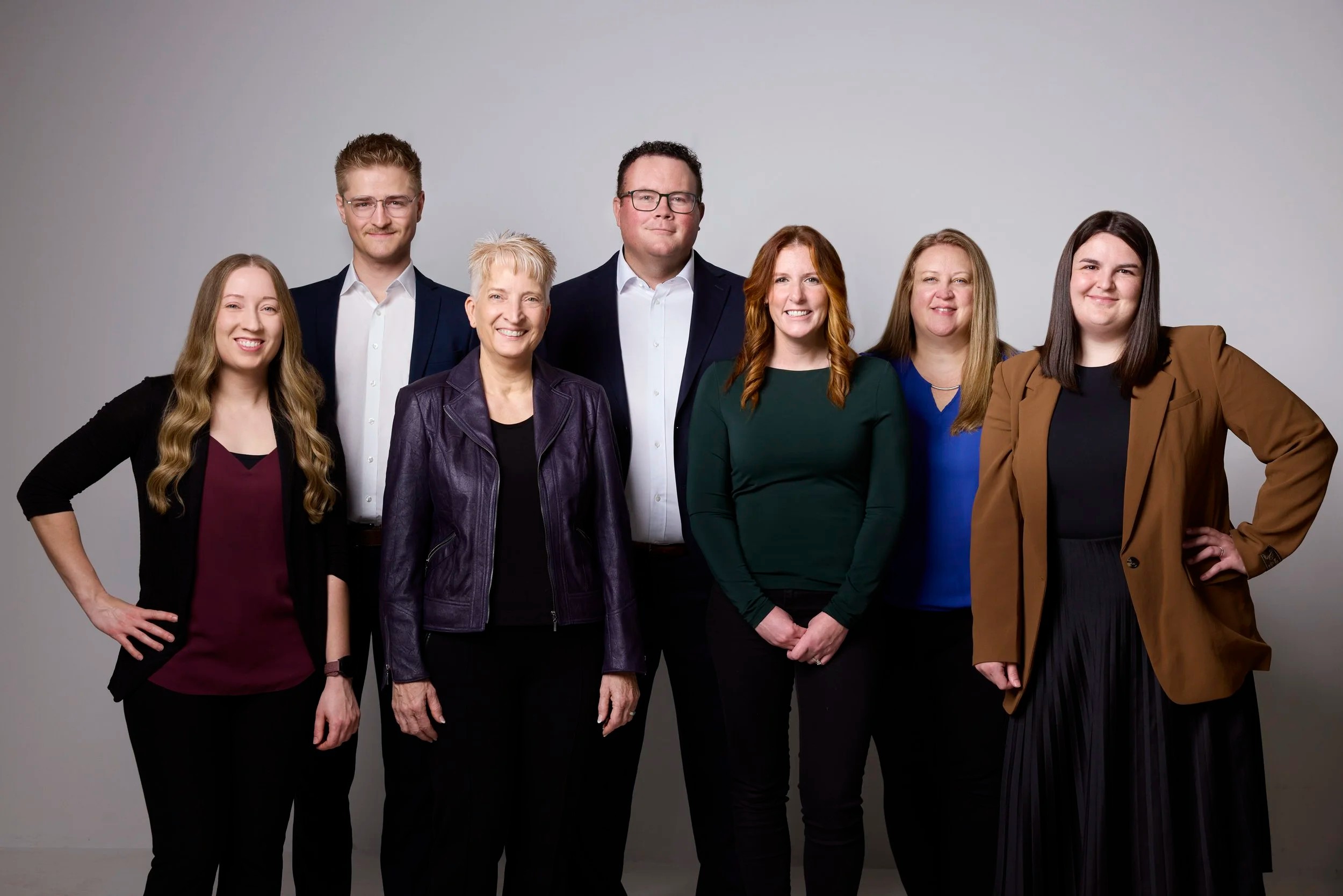 Group photo of a seven-person team on grey, Edmonton studio