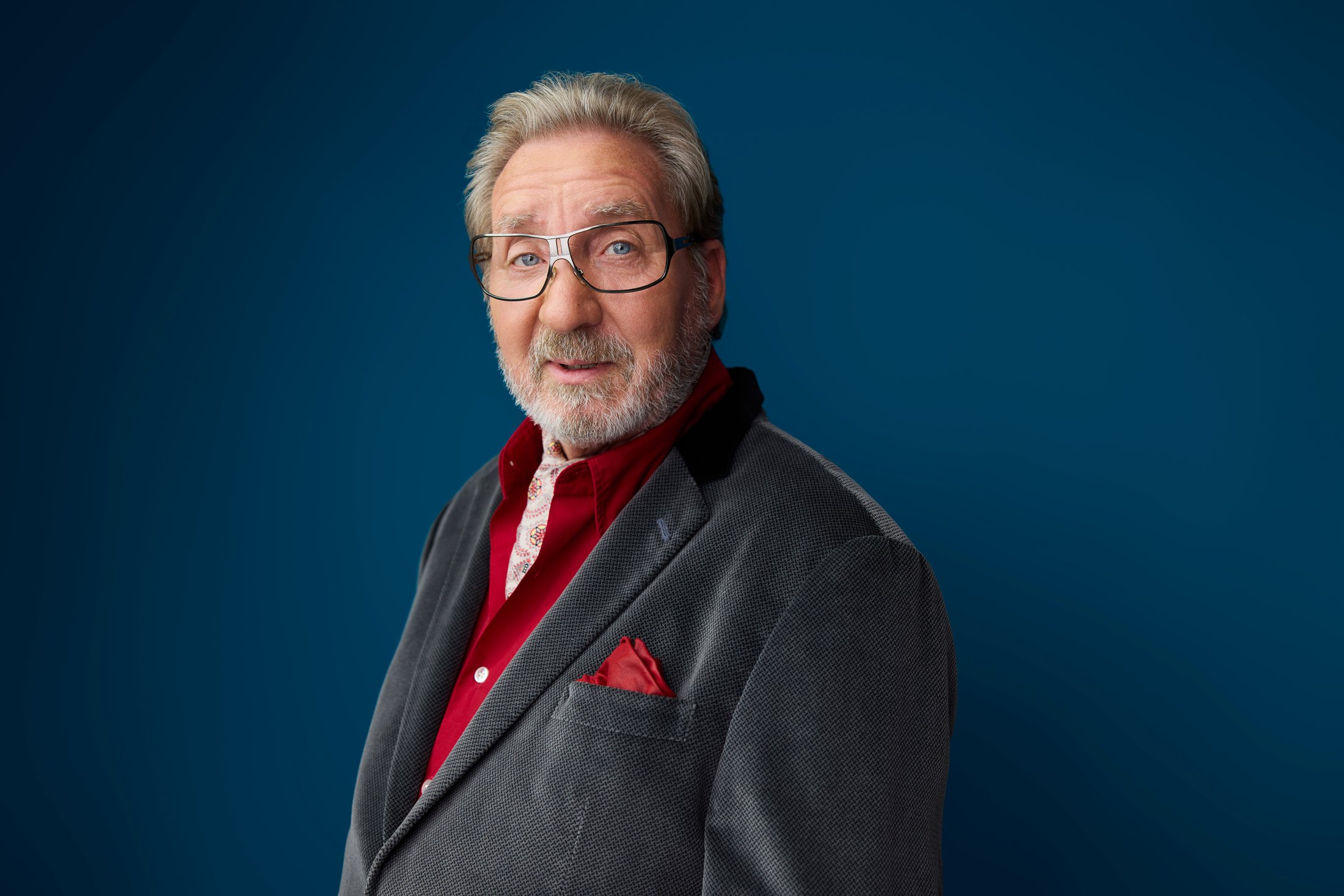 A man in a grey jacket and red pocket square against blue