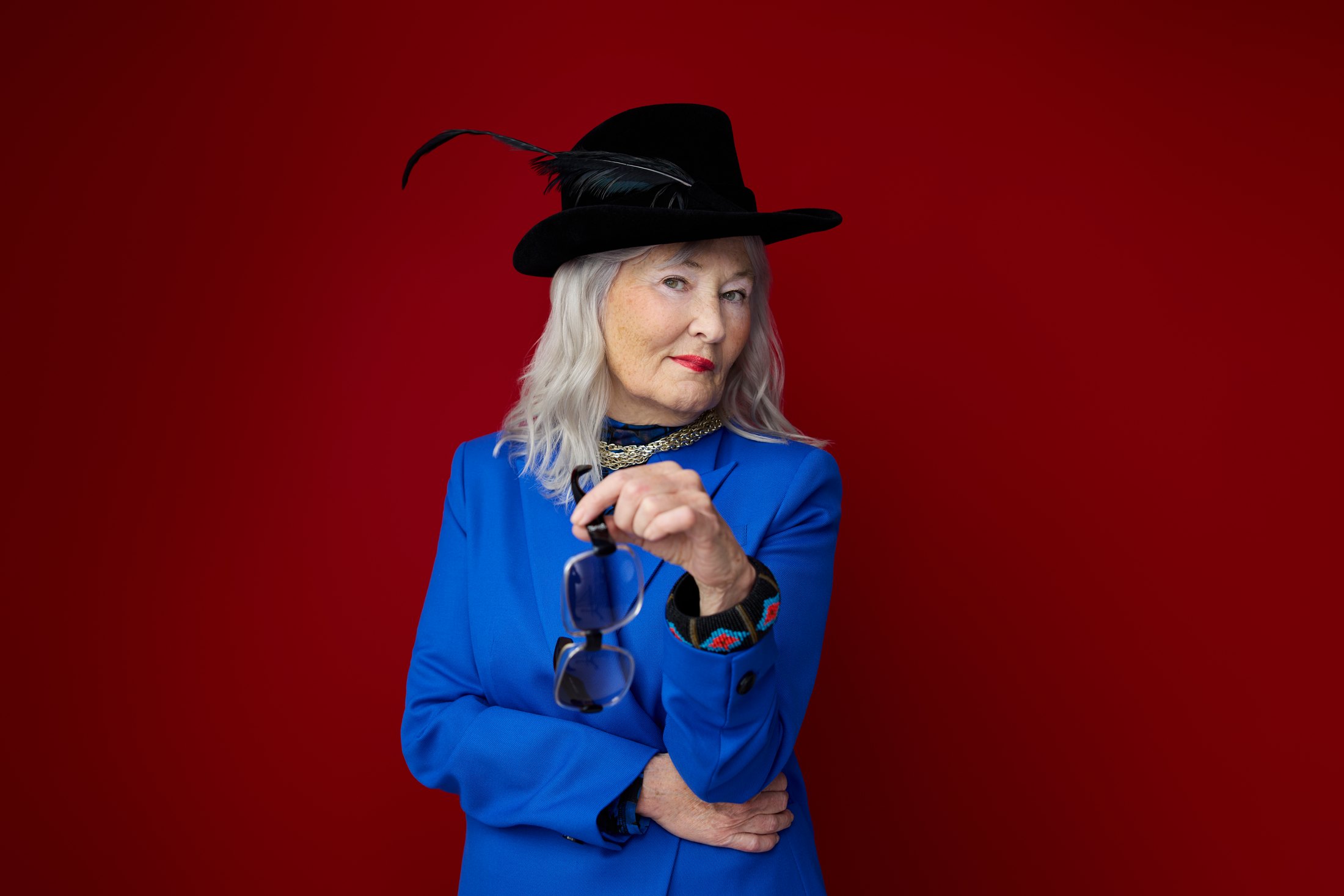 A woman in a wide-brimmed hat and blue jacket against red