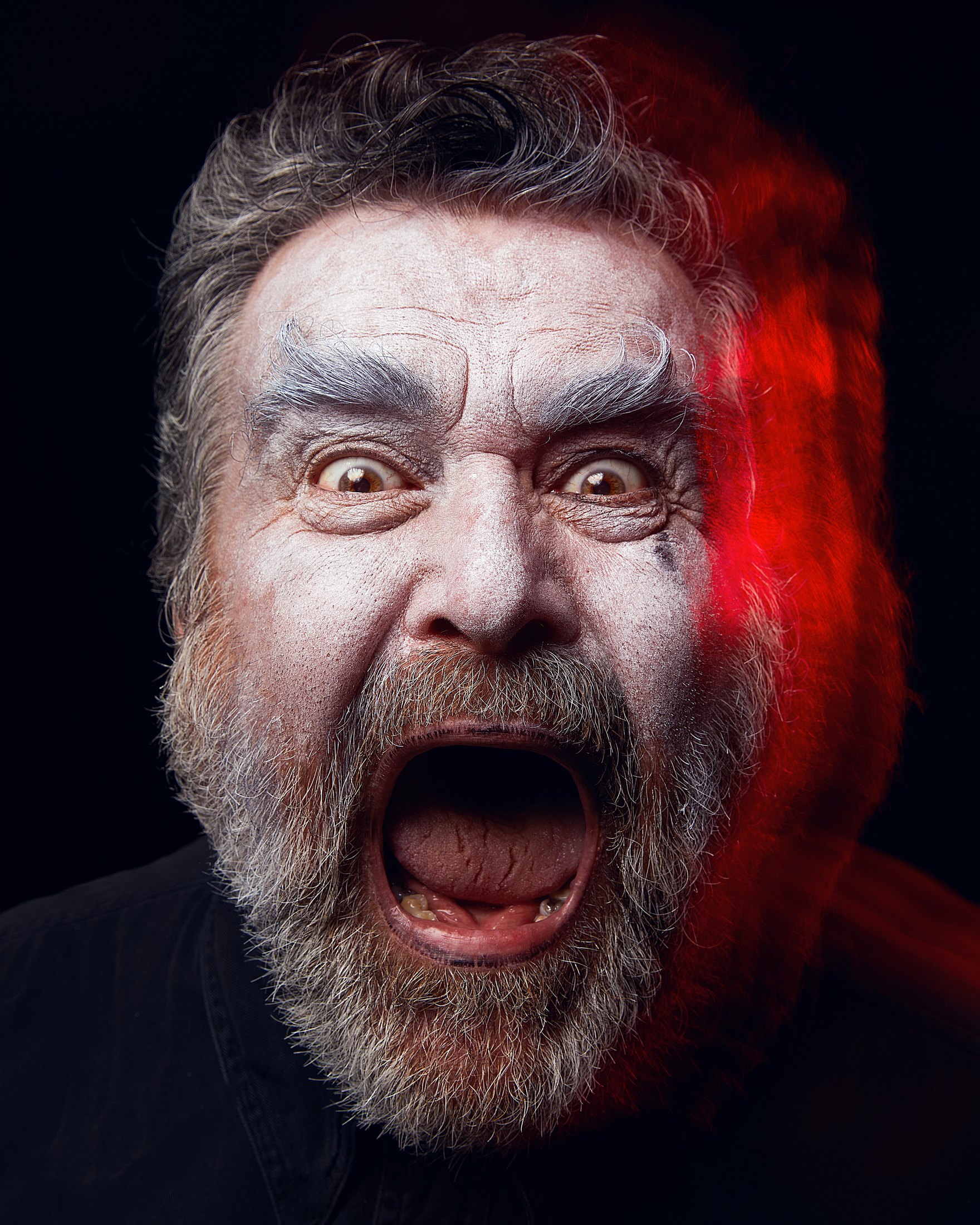 A bearded performer mid-shout, red light raking one side of his face