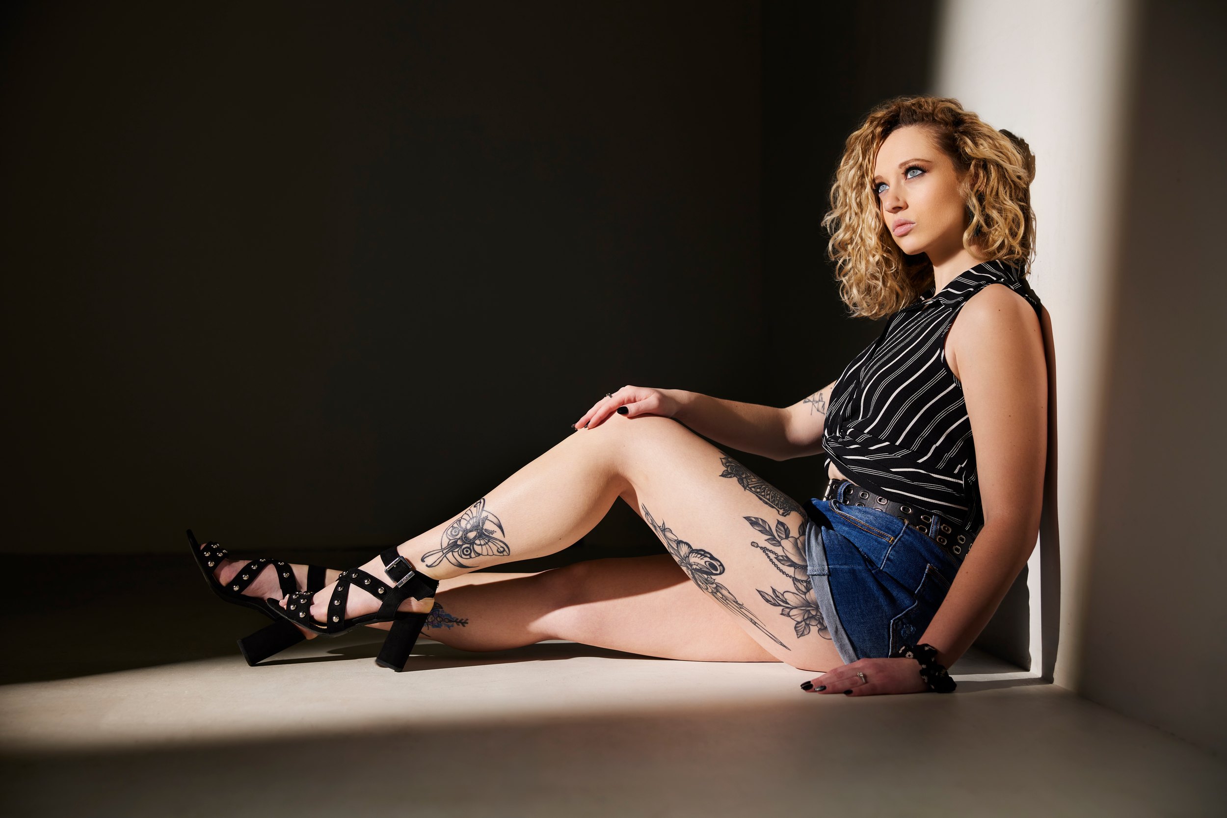 The same session, seated on the floor in a slit of light, striped top and denim shorts