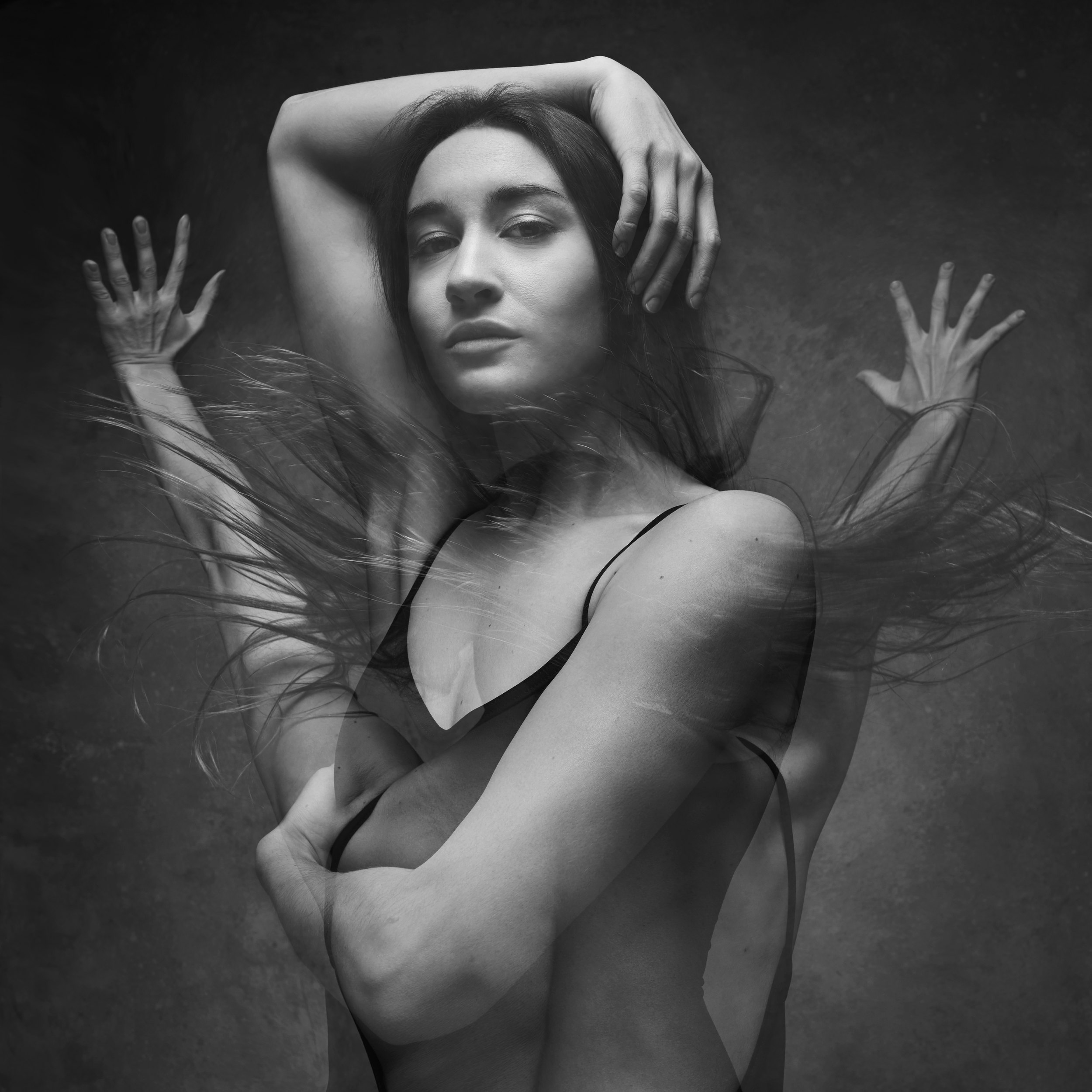 Black and white, several exposures at once: an arm over her head, hands spread, hair moving