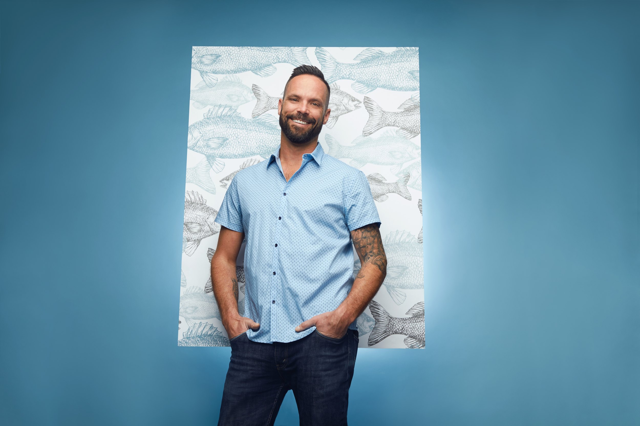 Rob Tryon in front of a panel of the fish-print wallpaper on blue, hands in his pockets