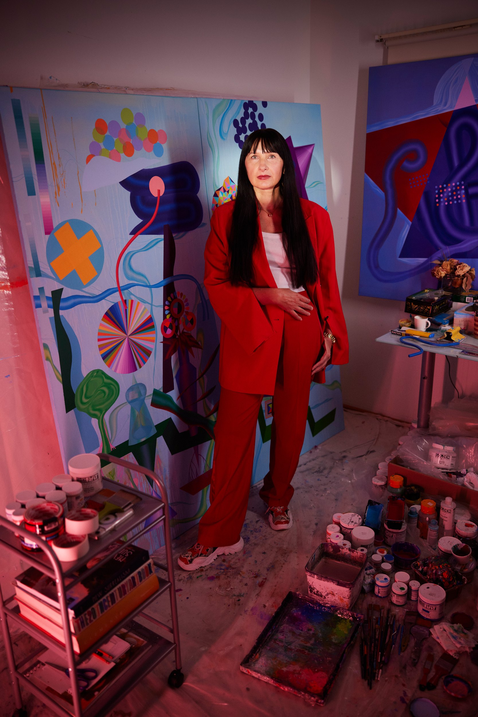 Oksana Movchan in a red suit in her studio, canvases on every wall