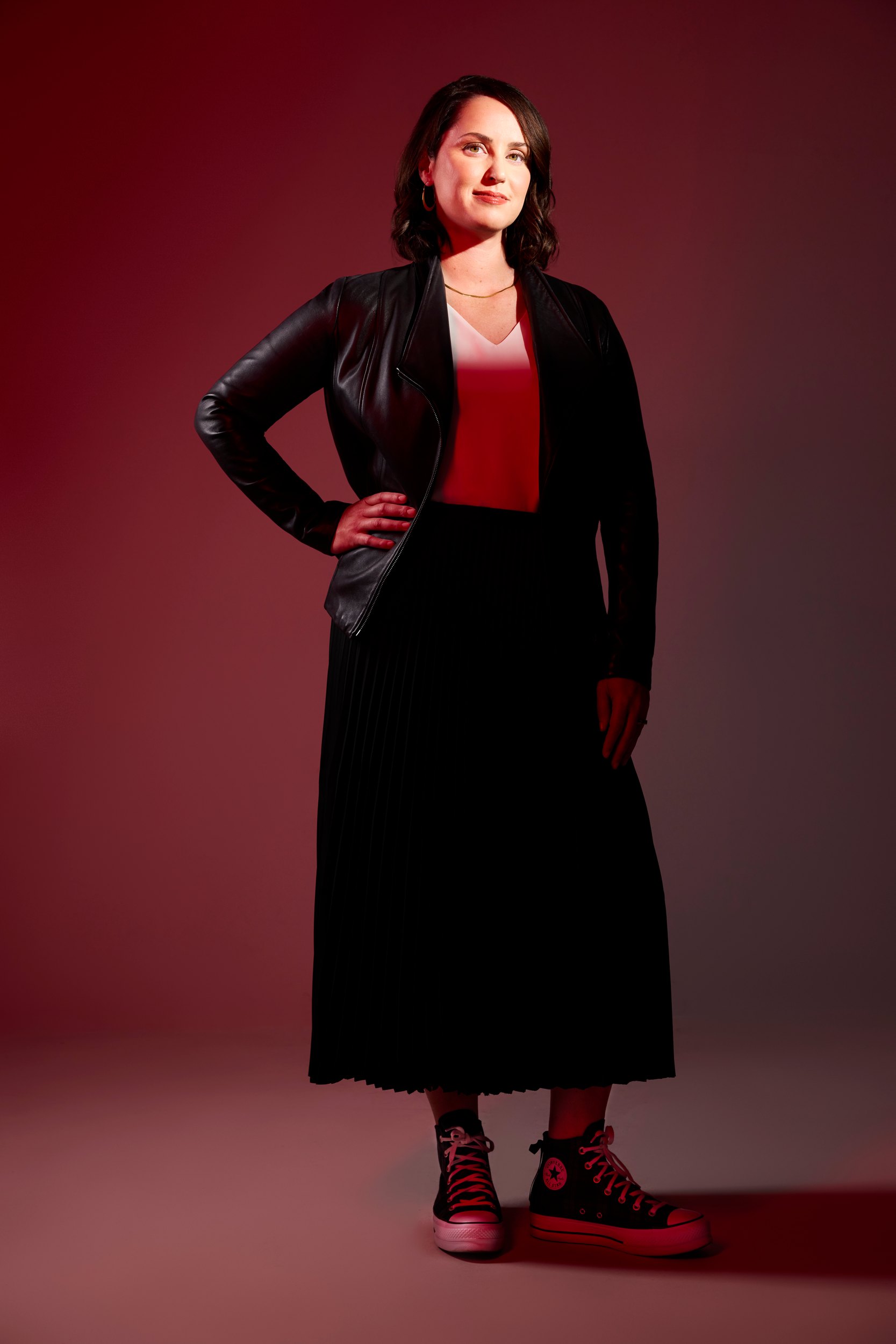 Sandra Stabel in a dark jacket and red top against crimson, a hand on her hip