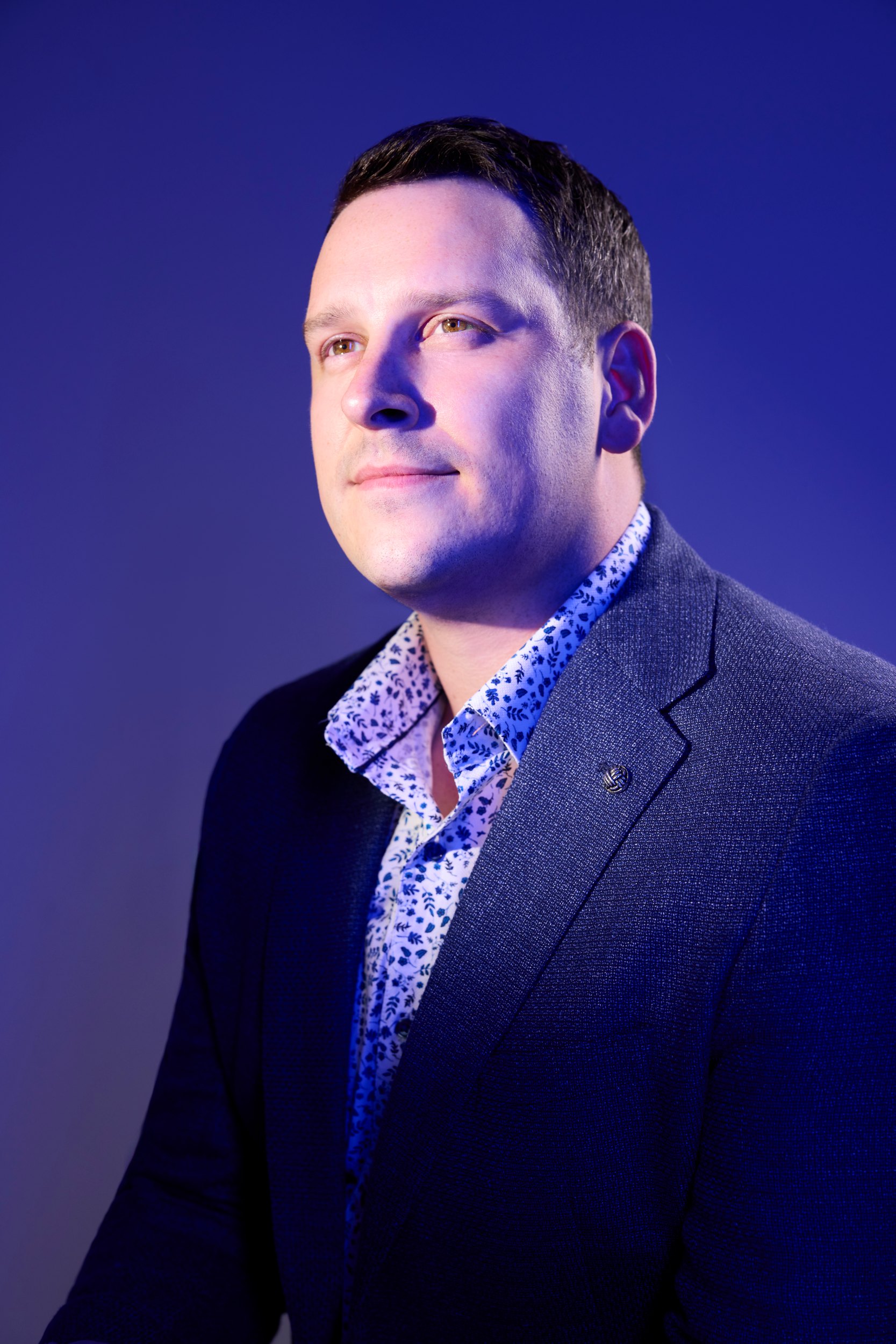 Scott Downey in a navy jacket and patterned shirt against deep blue