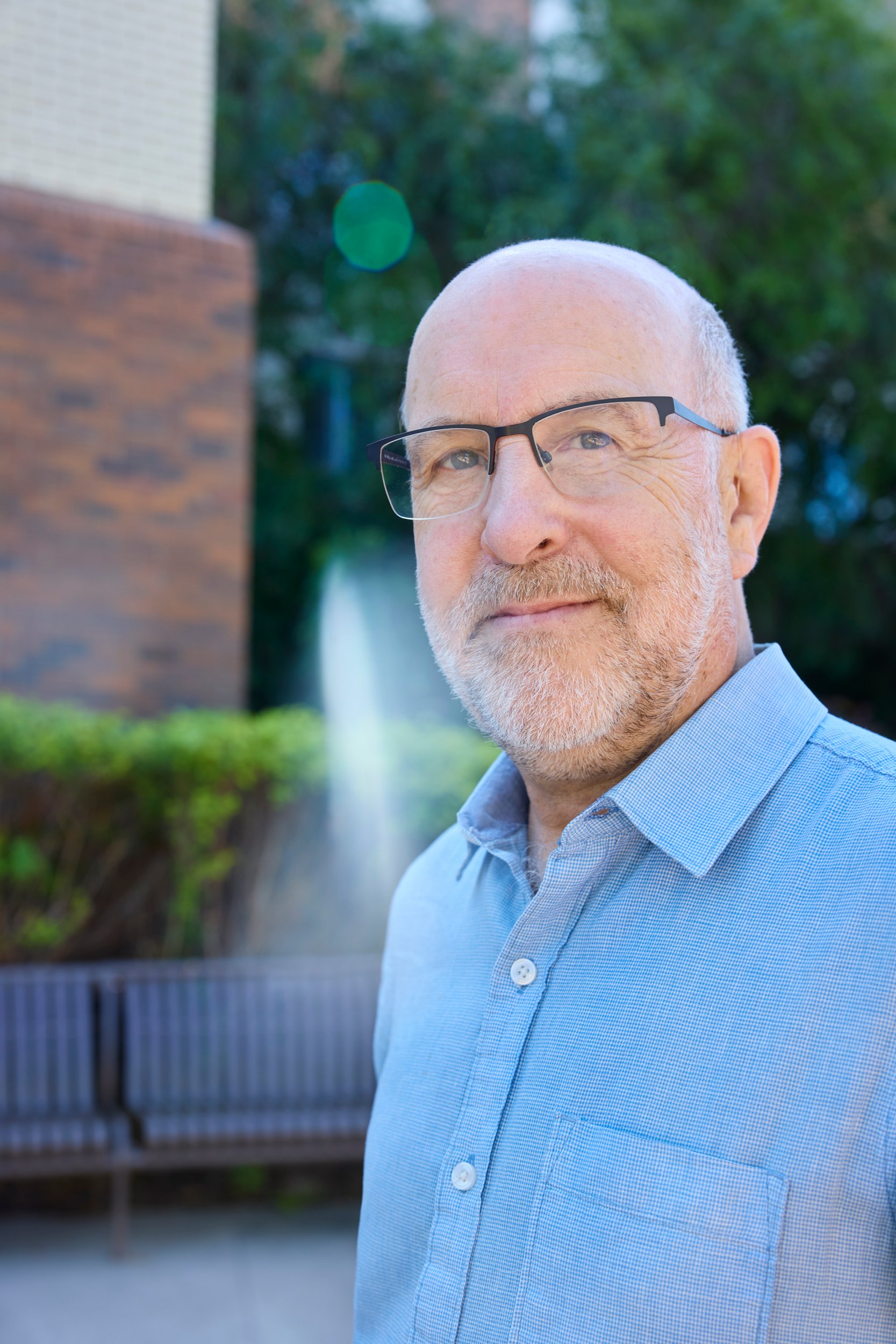 Dr. Michael Weinfeld outdoors in a blue shirt, looking off, a fountain behind him