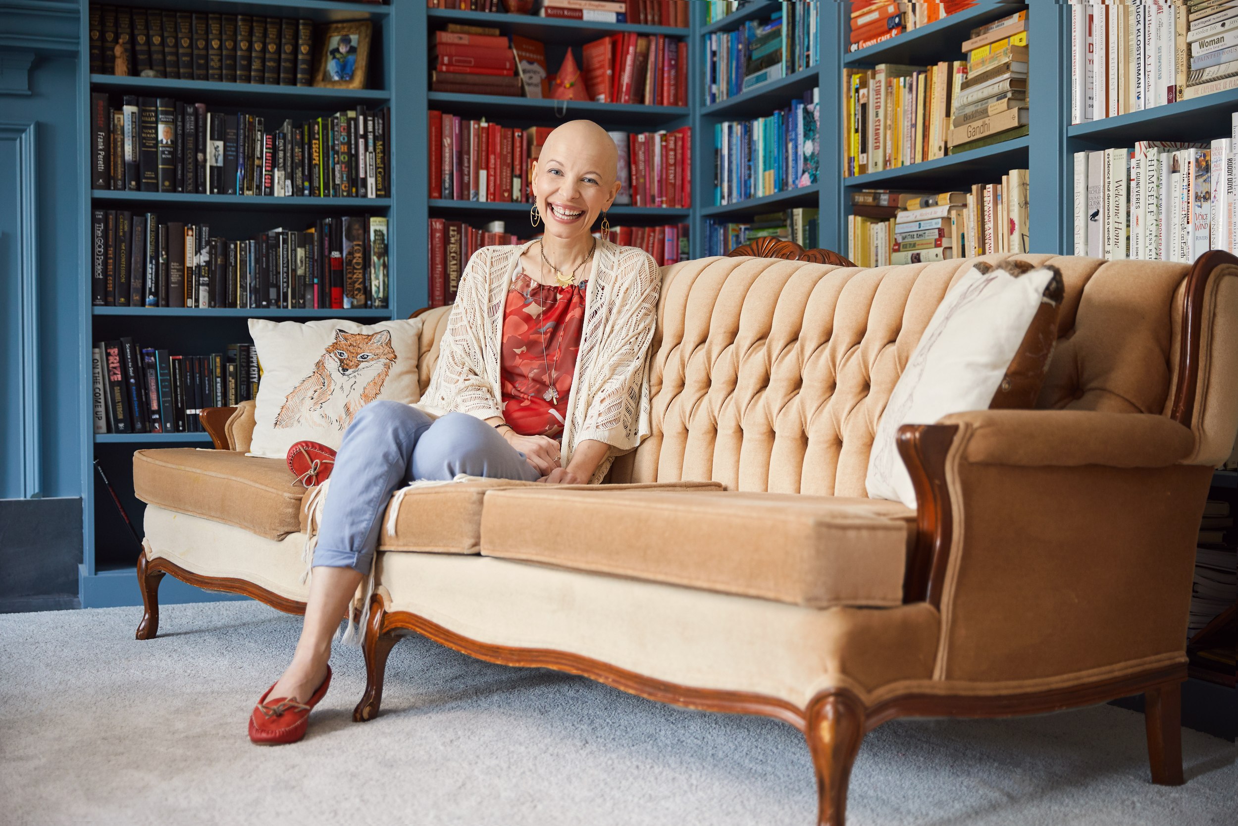 Julie Rohr on the sofa in front of the bookshelves, smiling to the lens