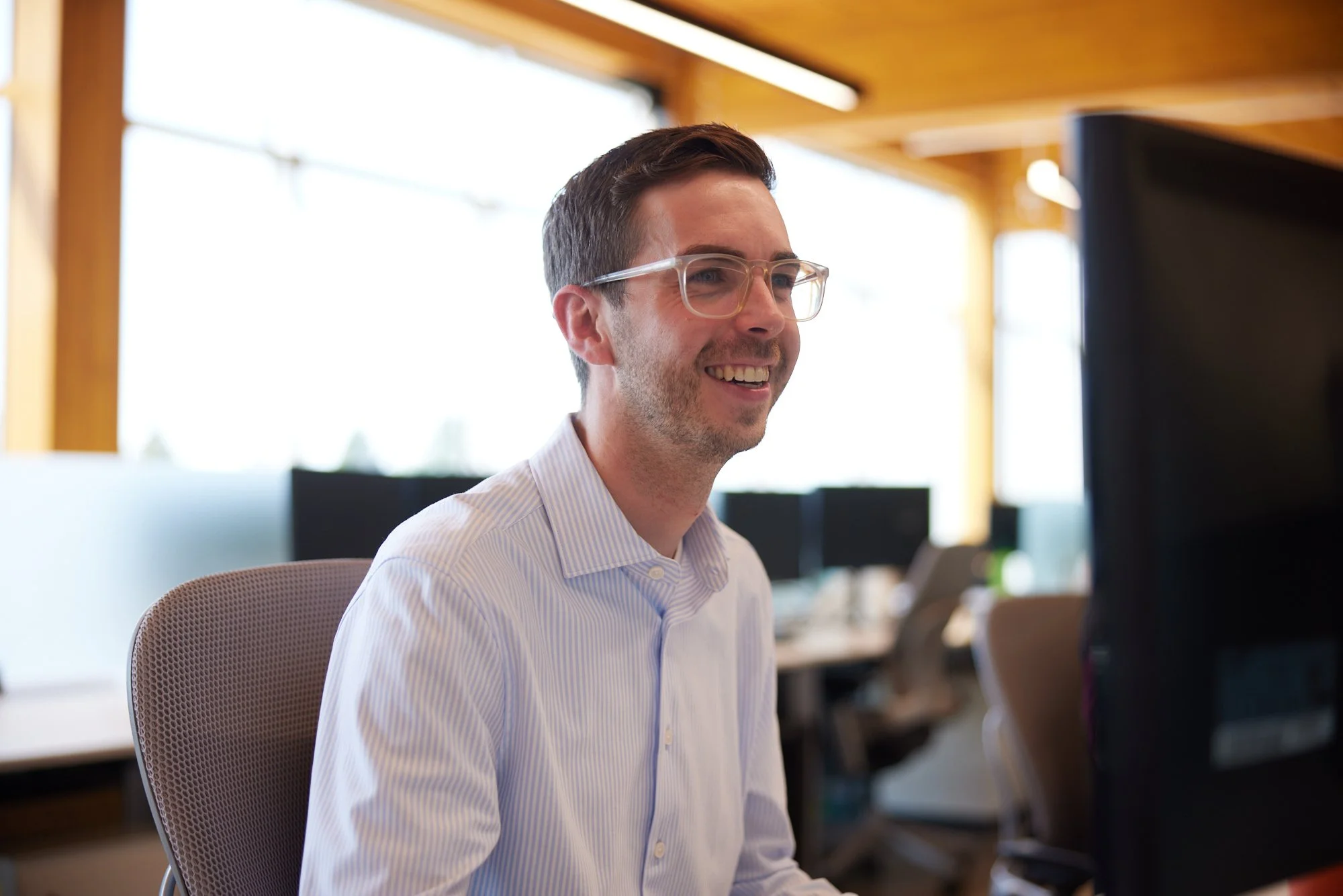 A man in glasses smiling at his monitor