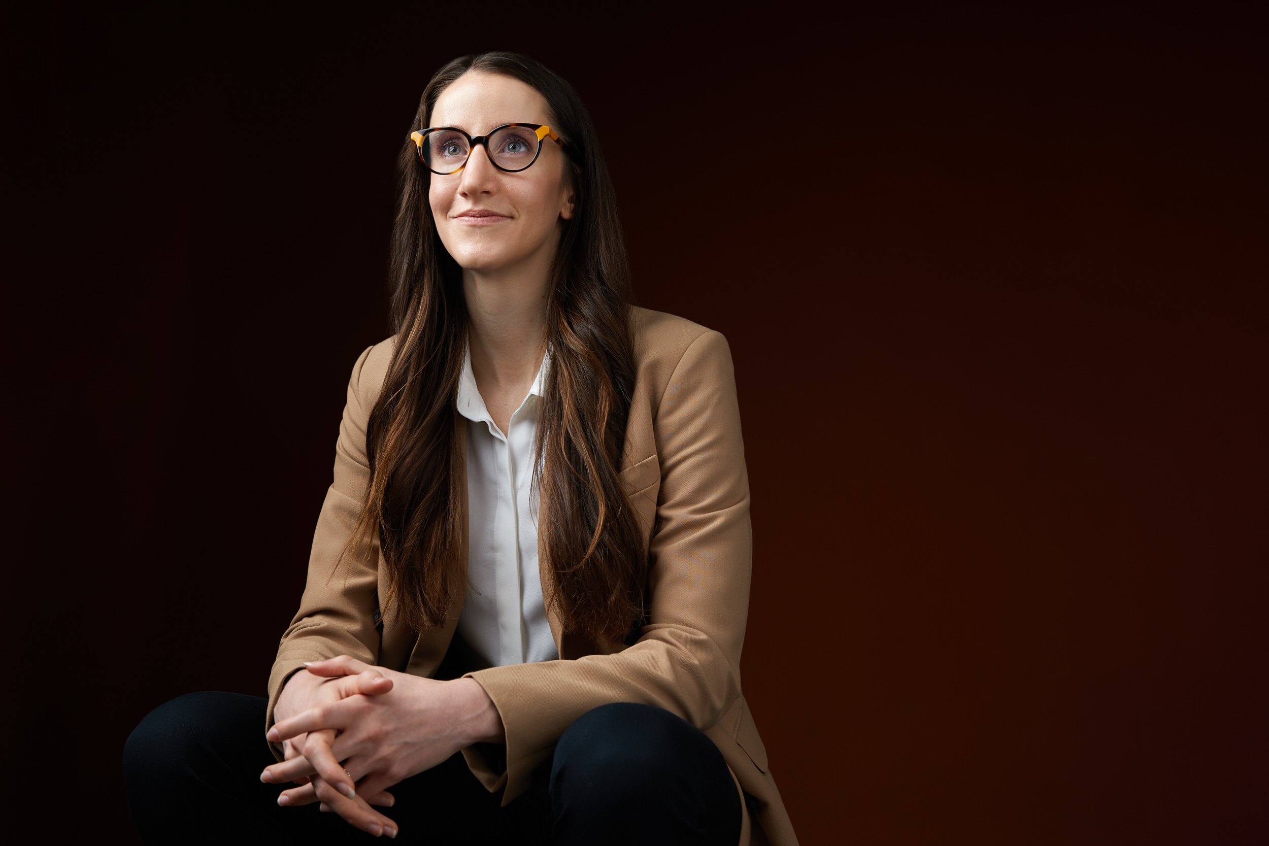 Executive portrait: seated in a camel blazer against a deep brown backdrop, Edmonton studio