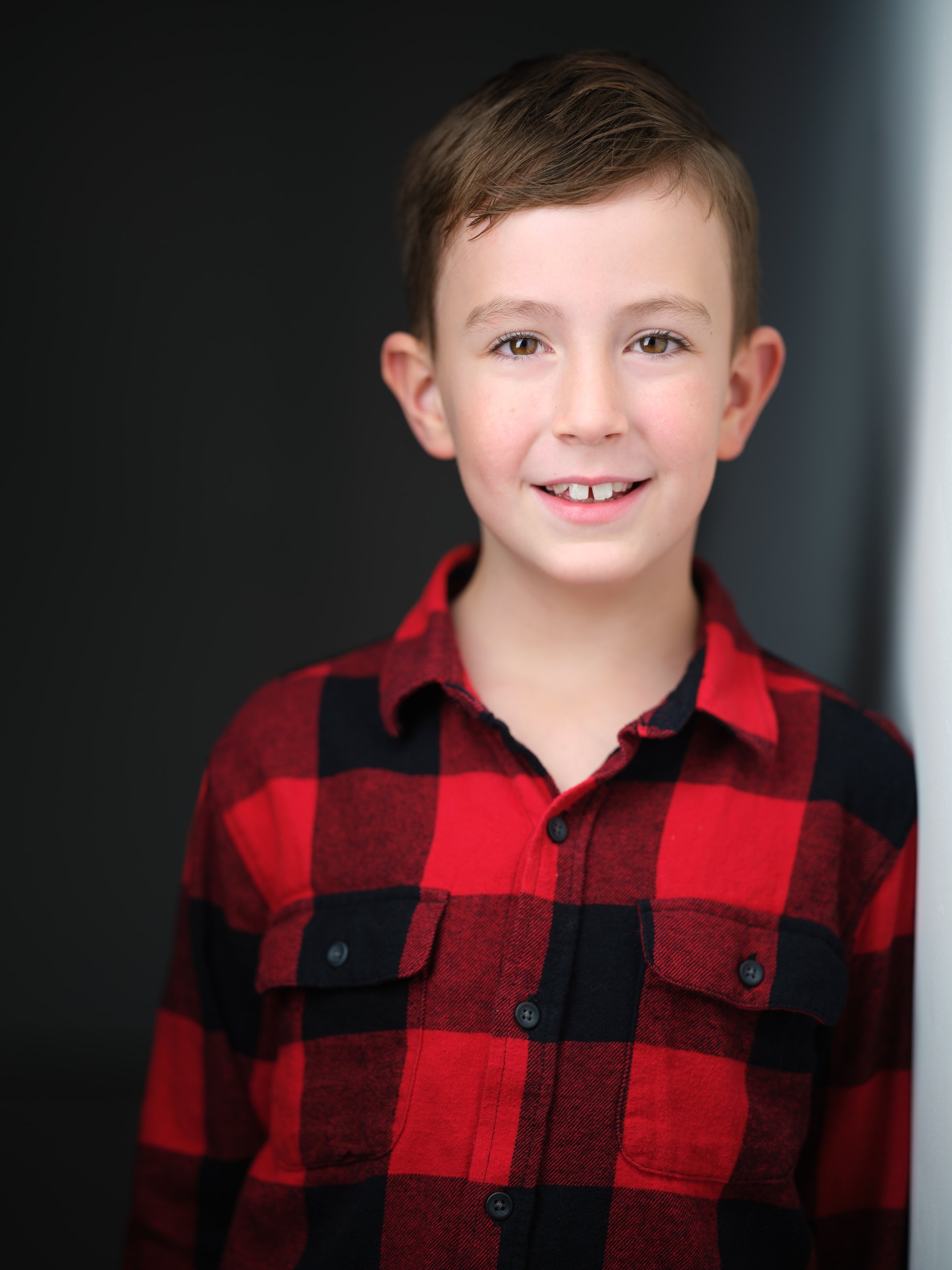 Kids and teens headshot: a red and black plaid shirt against the wall of light, grinning