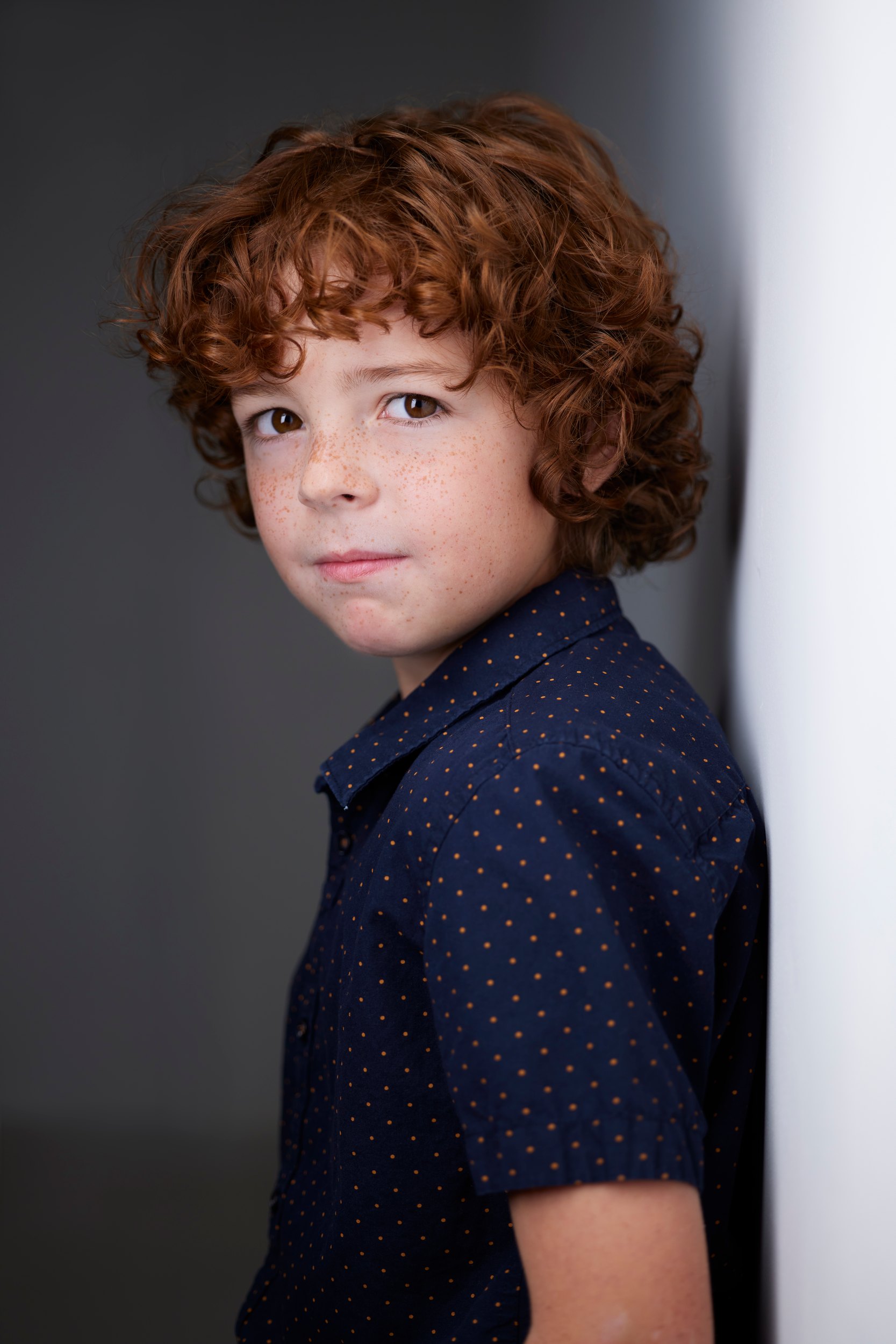Kids and teens headshot: a navy polka-dot shirt against the wall of light, red curls