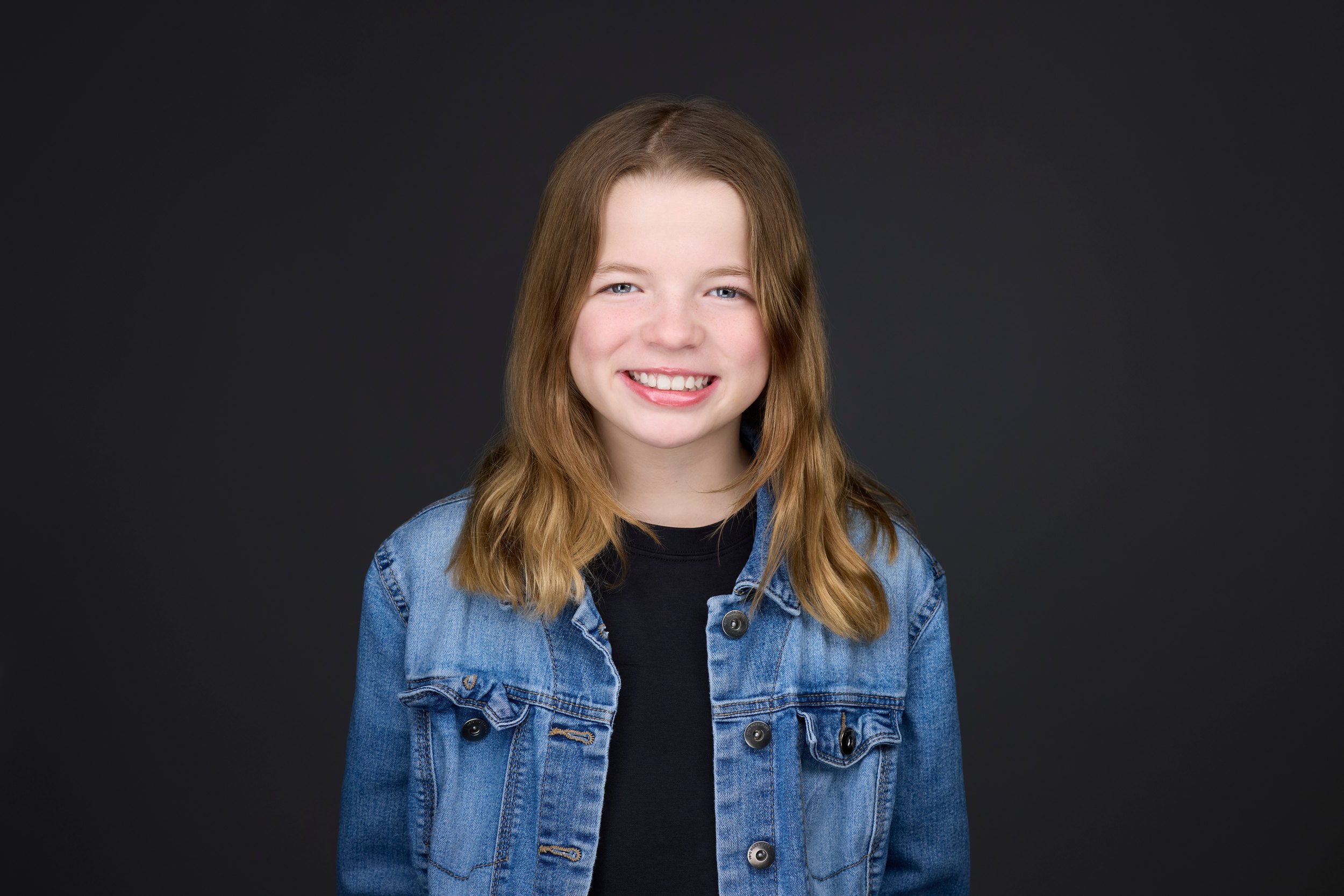 Kids and teens headshot: a denim jacket over black against black, smiling