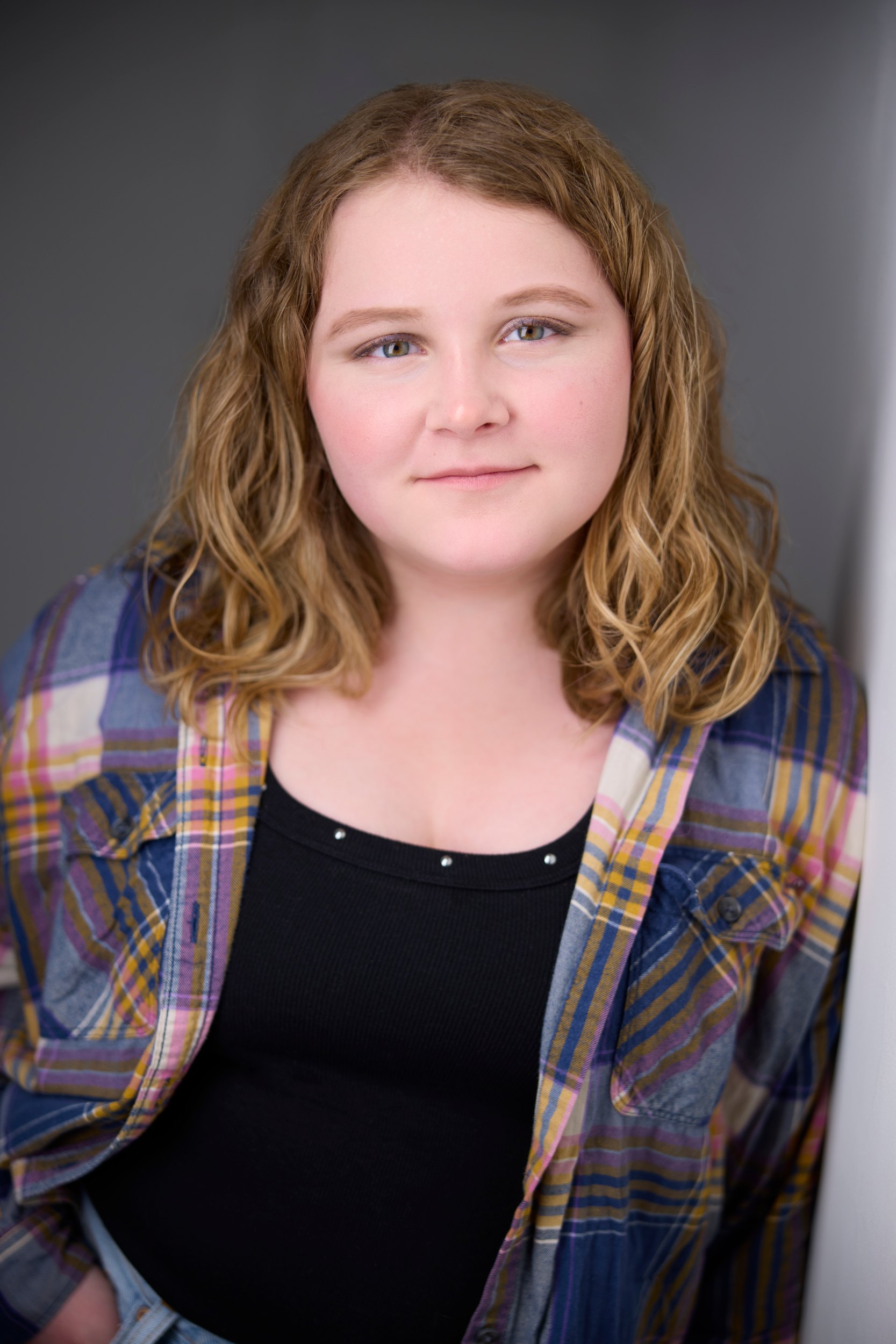 Kids and teens headshot: a plaid shirt over black against the wall of light, curls