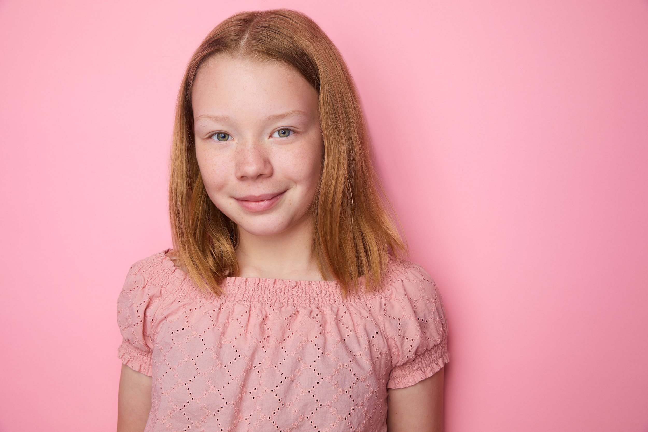 Kids and teens headshot: a pink eyelet top against pink, red hair