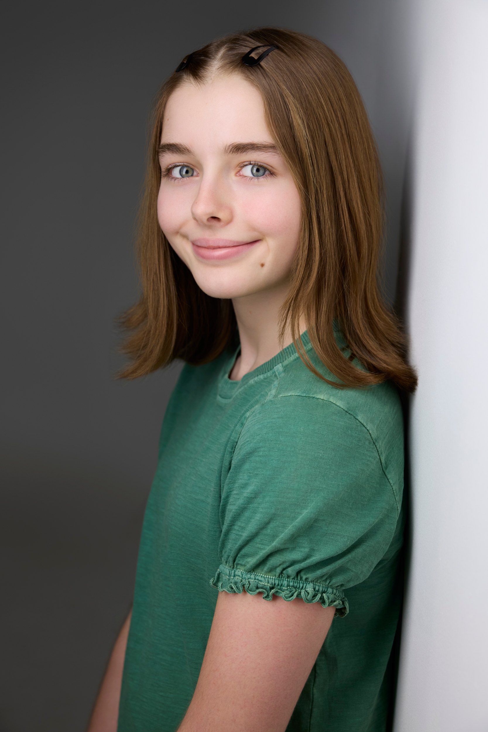 Kids and teens headshot: a green tee against the wall of light, smiling