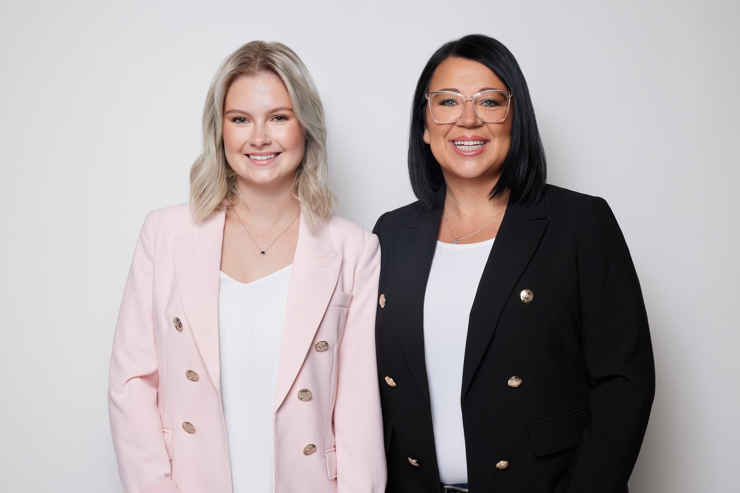 Two real estate agents side by side, a pink blazer and a black blazer, on white