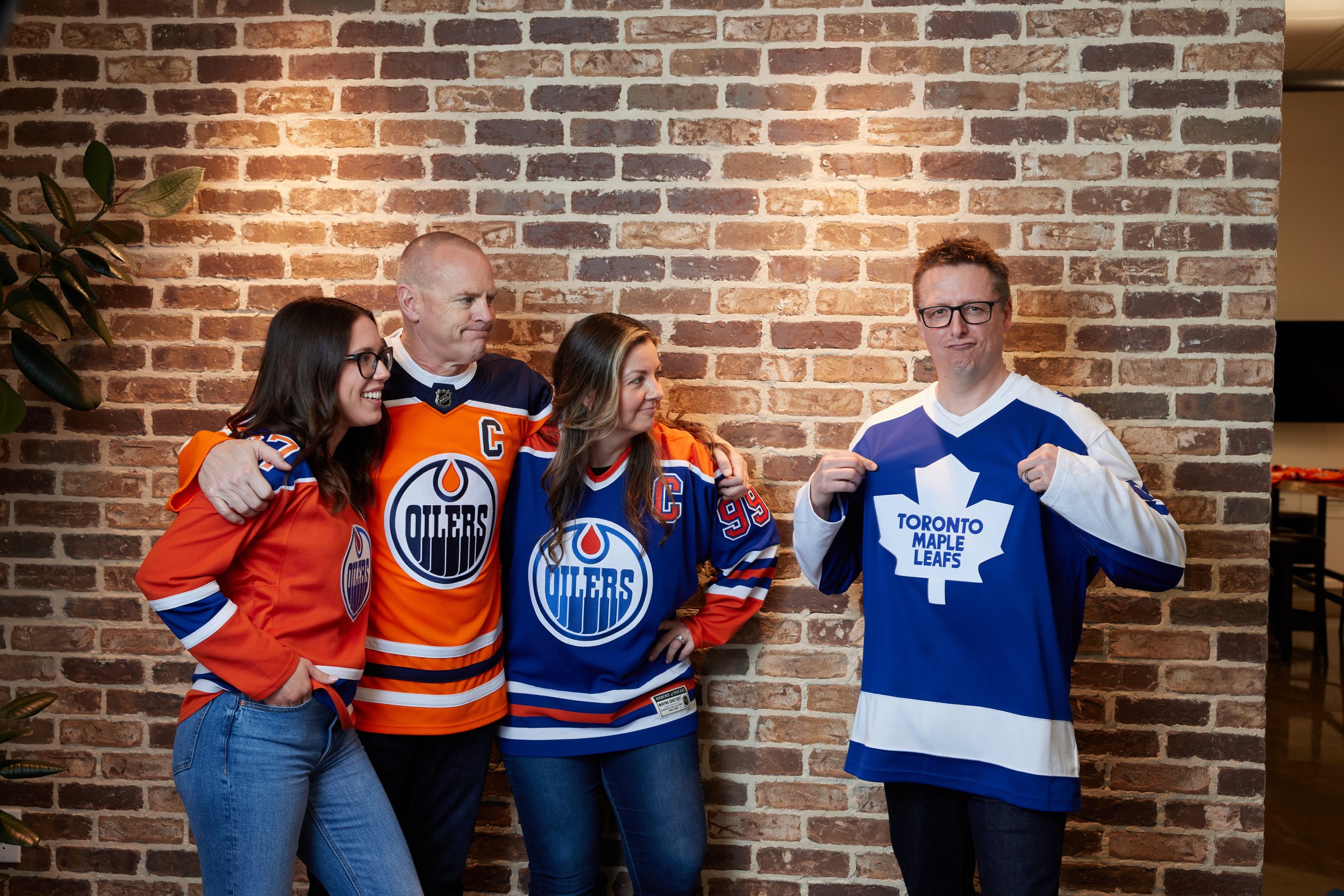 The same team against a brick wall in Oilers jerseys, three of them leaning away from the one in a Maple Leafs jersey