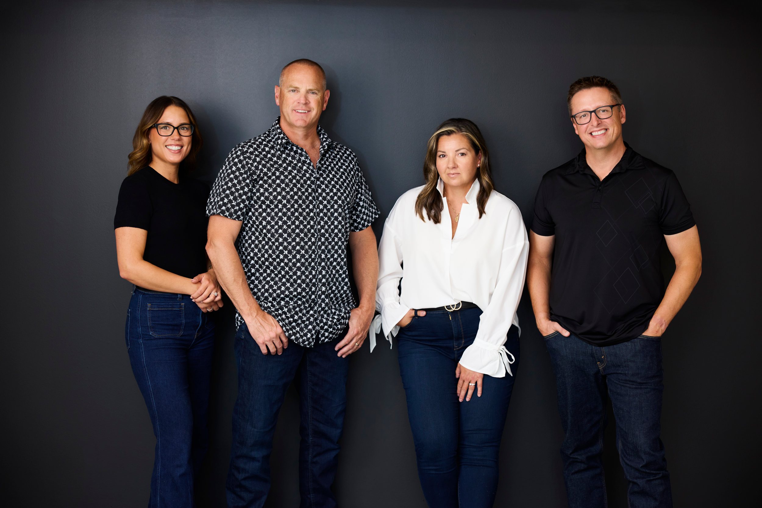 A real estate team of four standing against the dark wall of their office