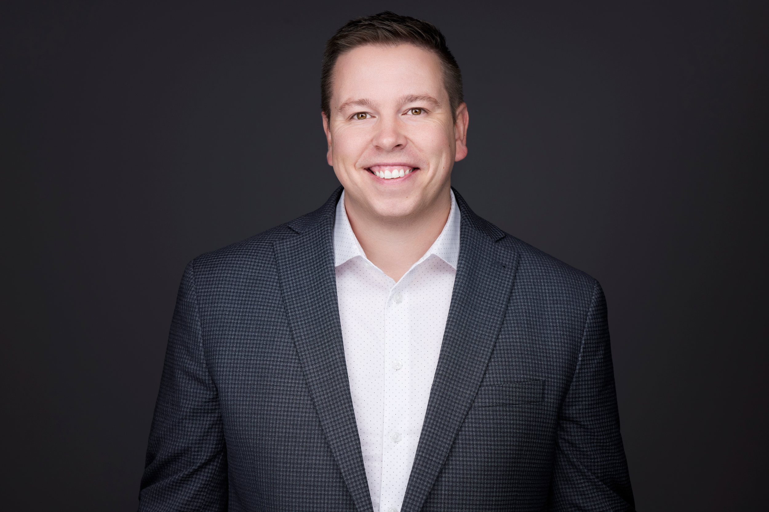 Real estate headshot: a charcoal suit and an open white collar, smiling, on dark