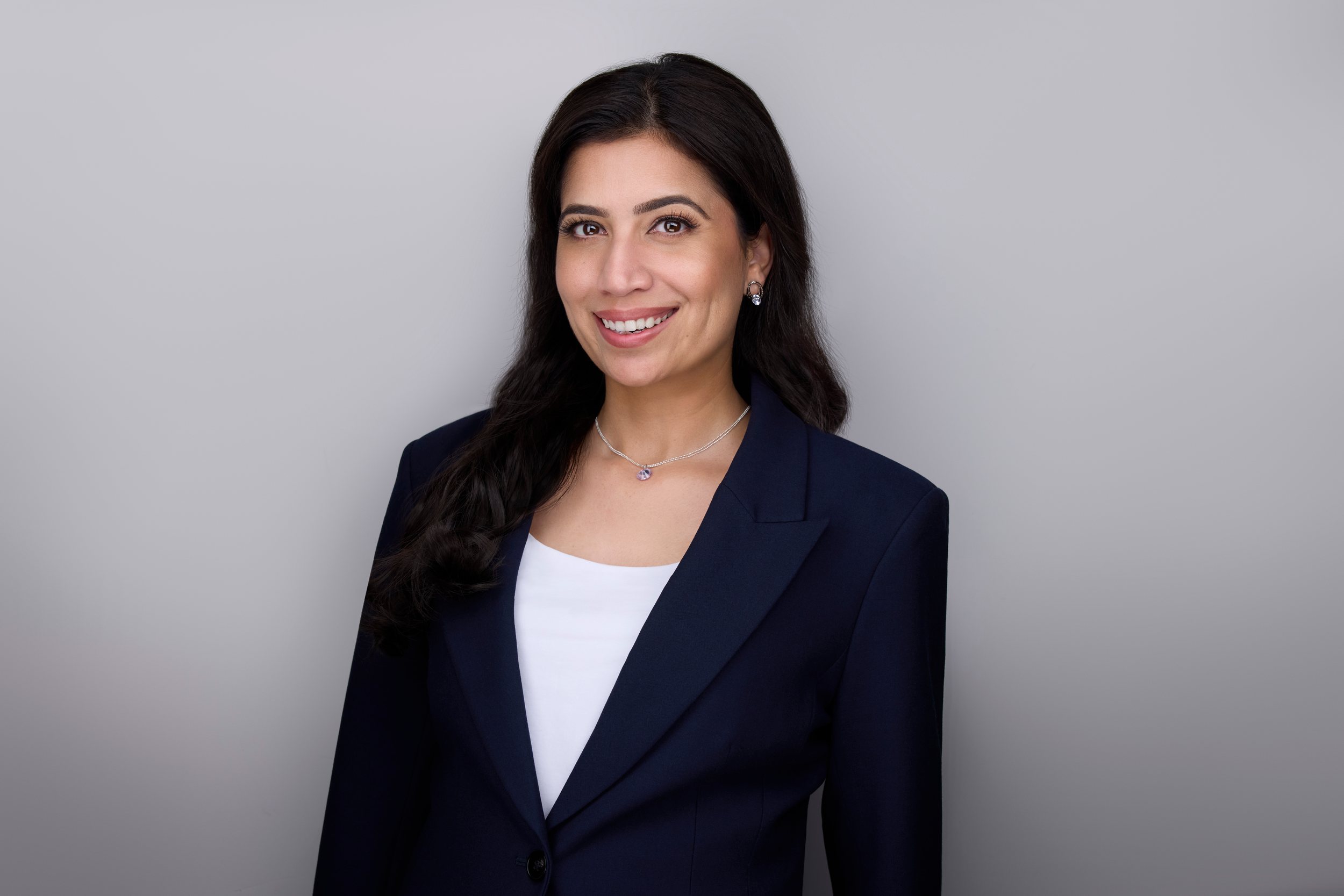 Real estate headshot: long dark hair, a navy blazer over white, on light grey