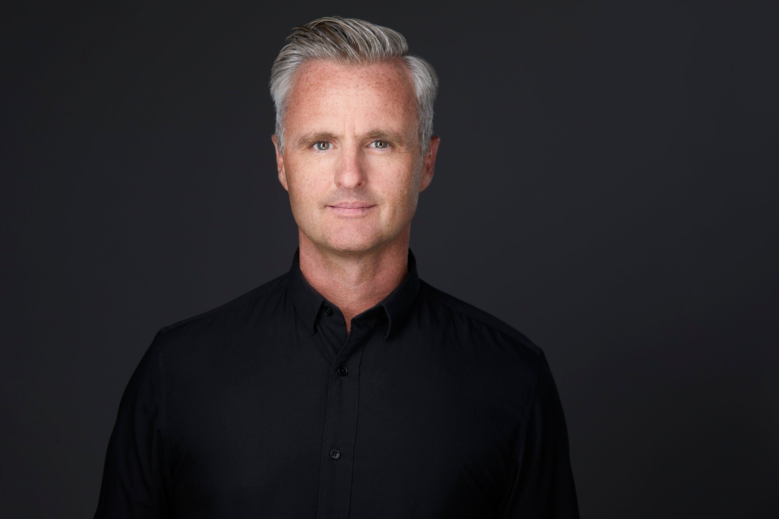 Real estate headshot: silver hair, a black shirt, on dark