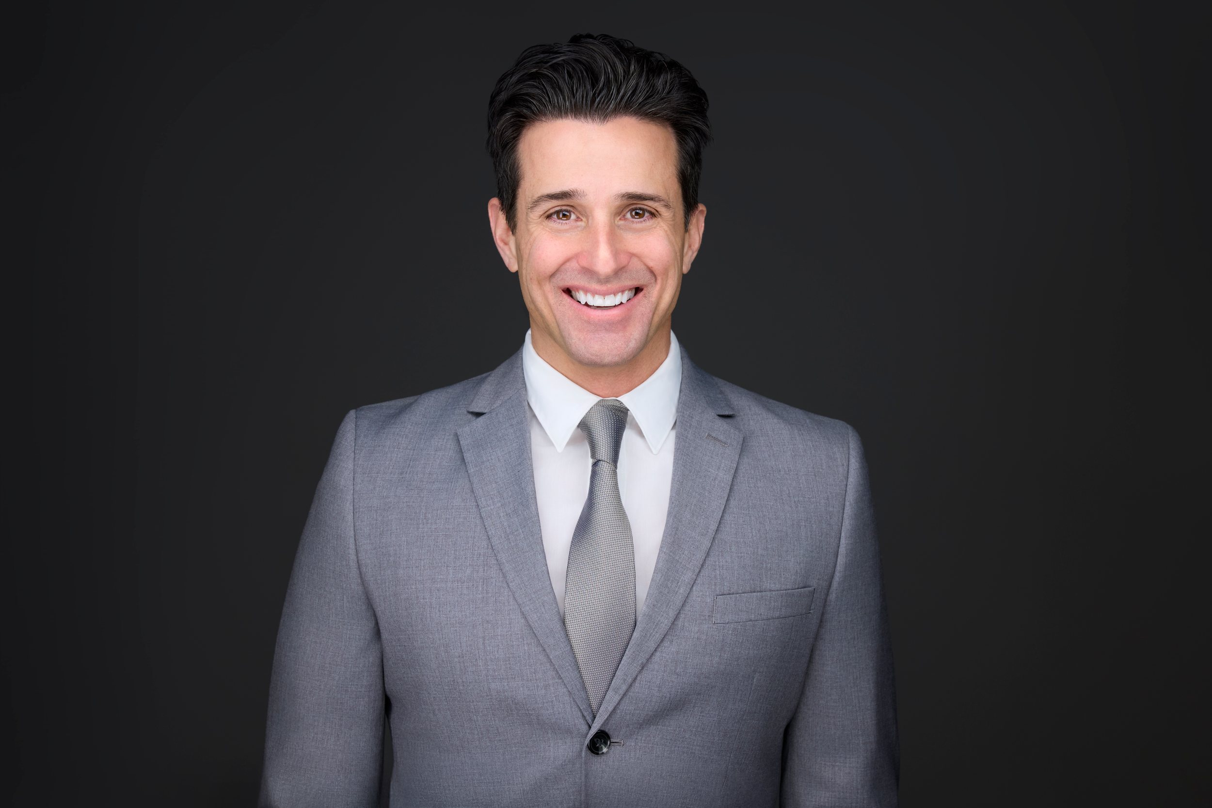 Real estate headshot: a light grey suit and tie, smiling, on dark