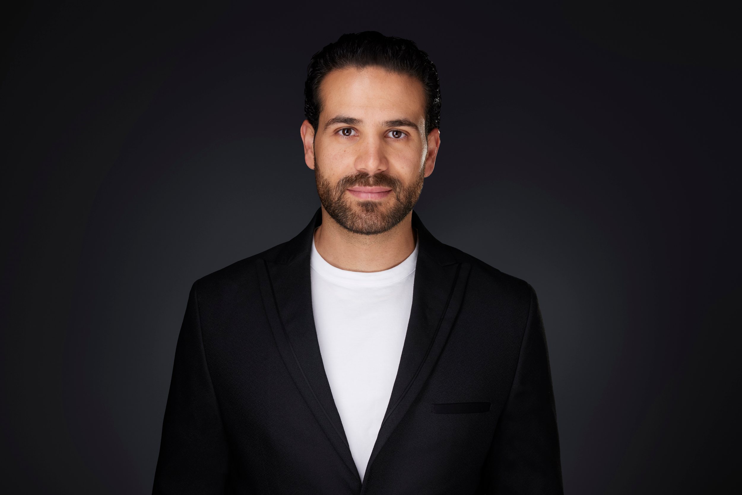 Real estate headshot: a beard, a black blazer over a white T-shirt, on dark
