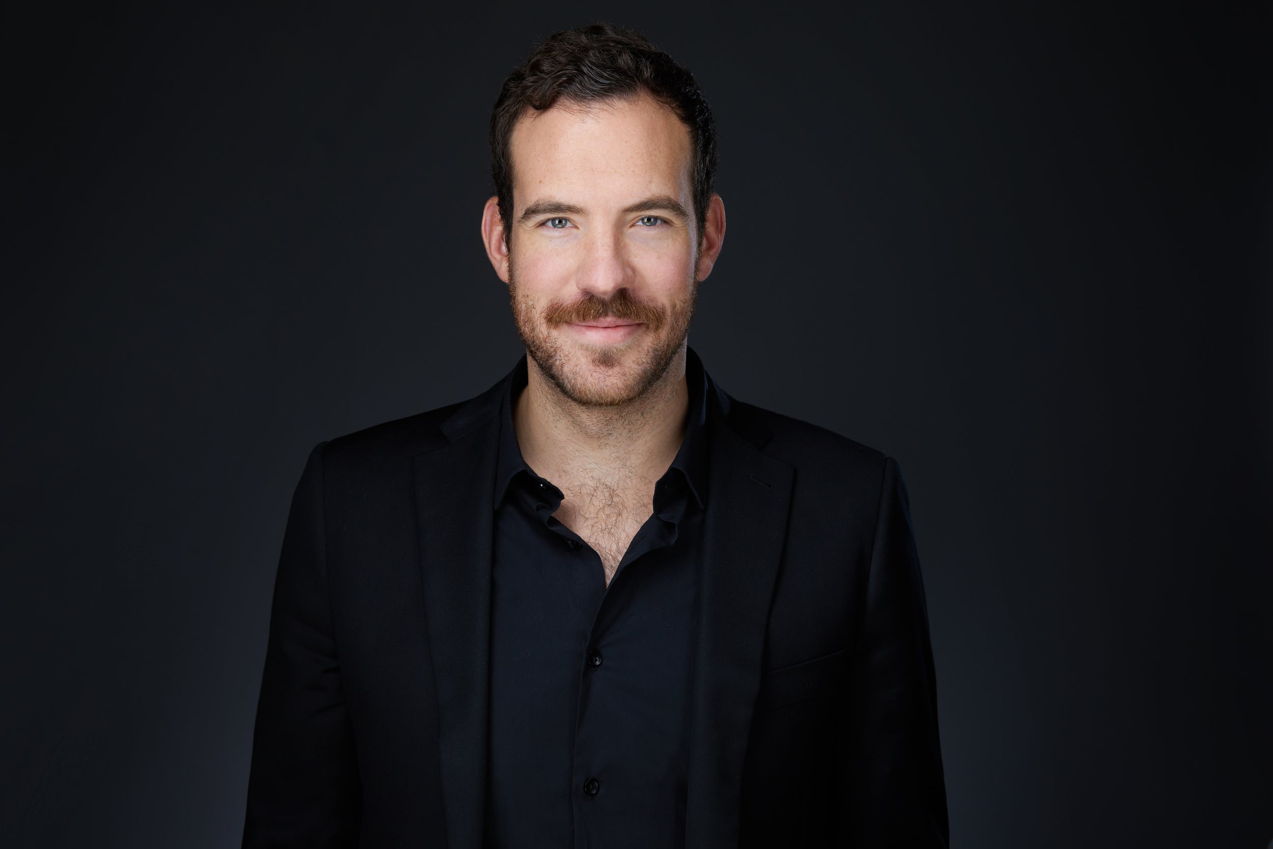 Real estate headshot: a beard, a black jacket and an open black shirt, on dark