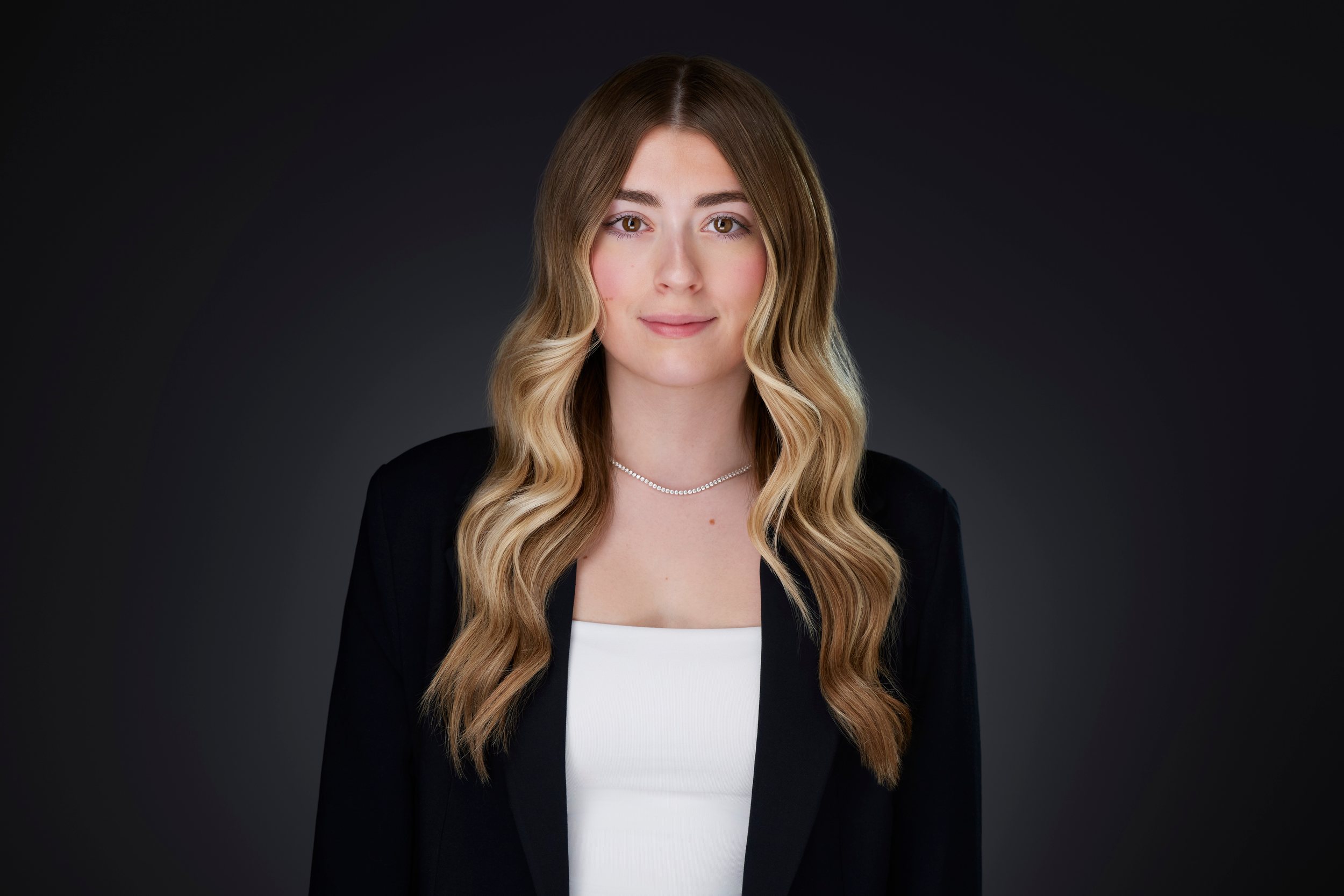 Real estate headshot: long blonde waves, a black blazer over white, on dark