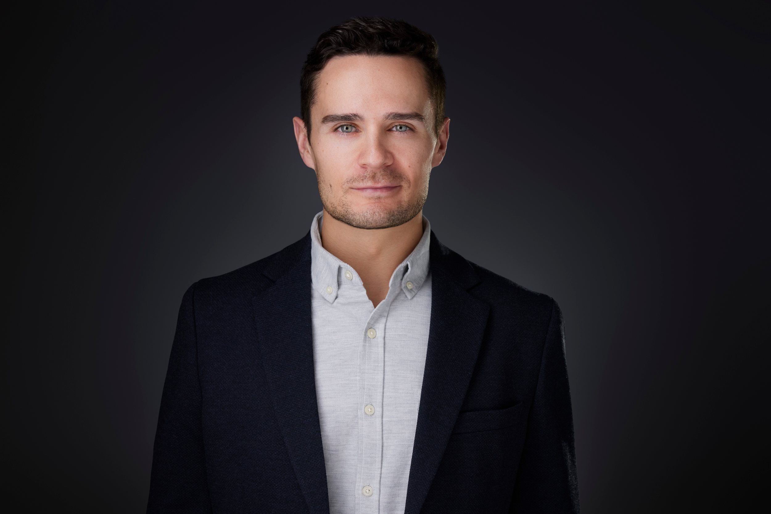 Real estate headshot: a black blazer over a grey shirt, on dark