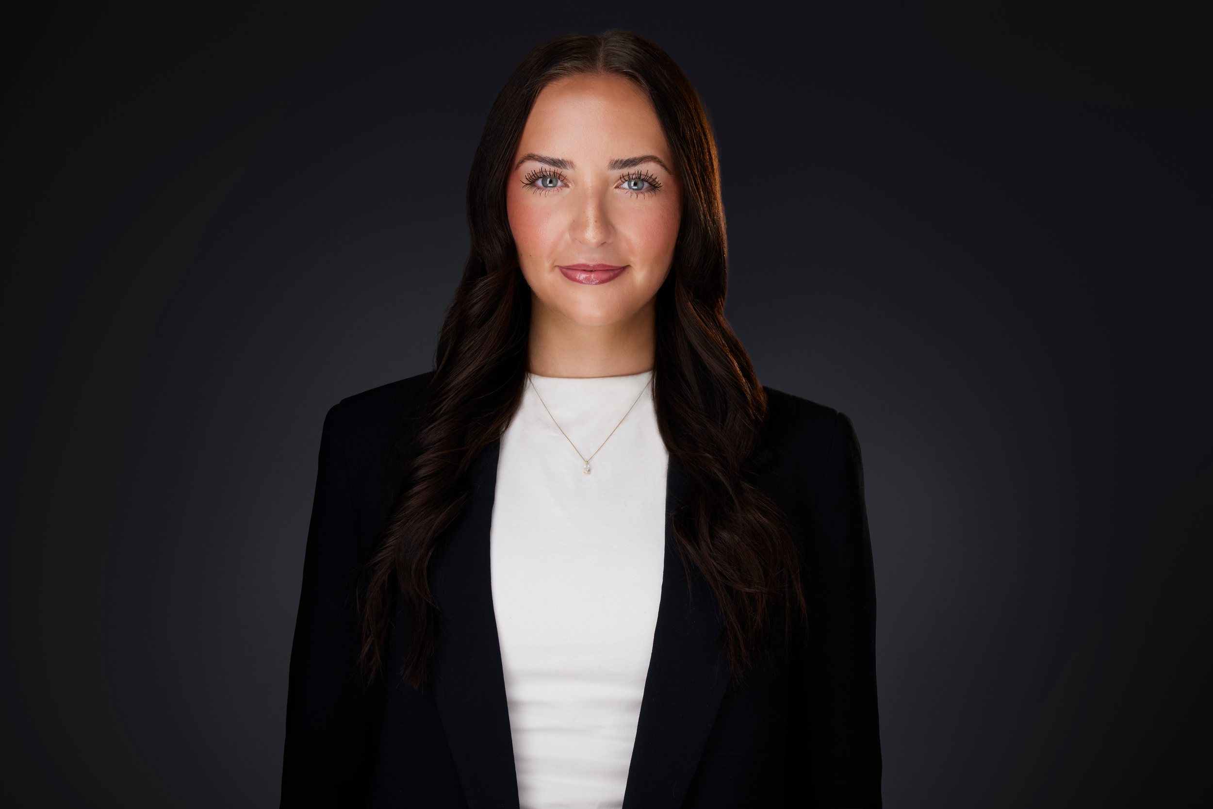 Real estate headshot: long dark hair, a black blazer over white, on dark