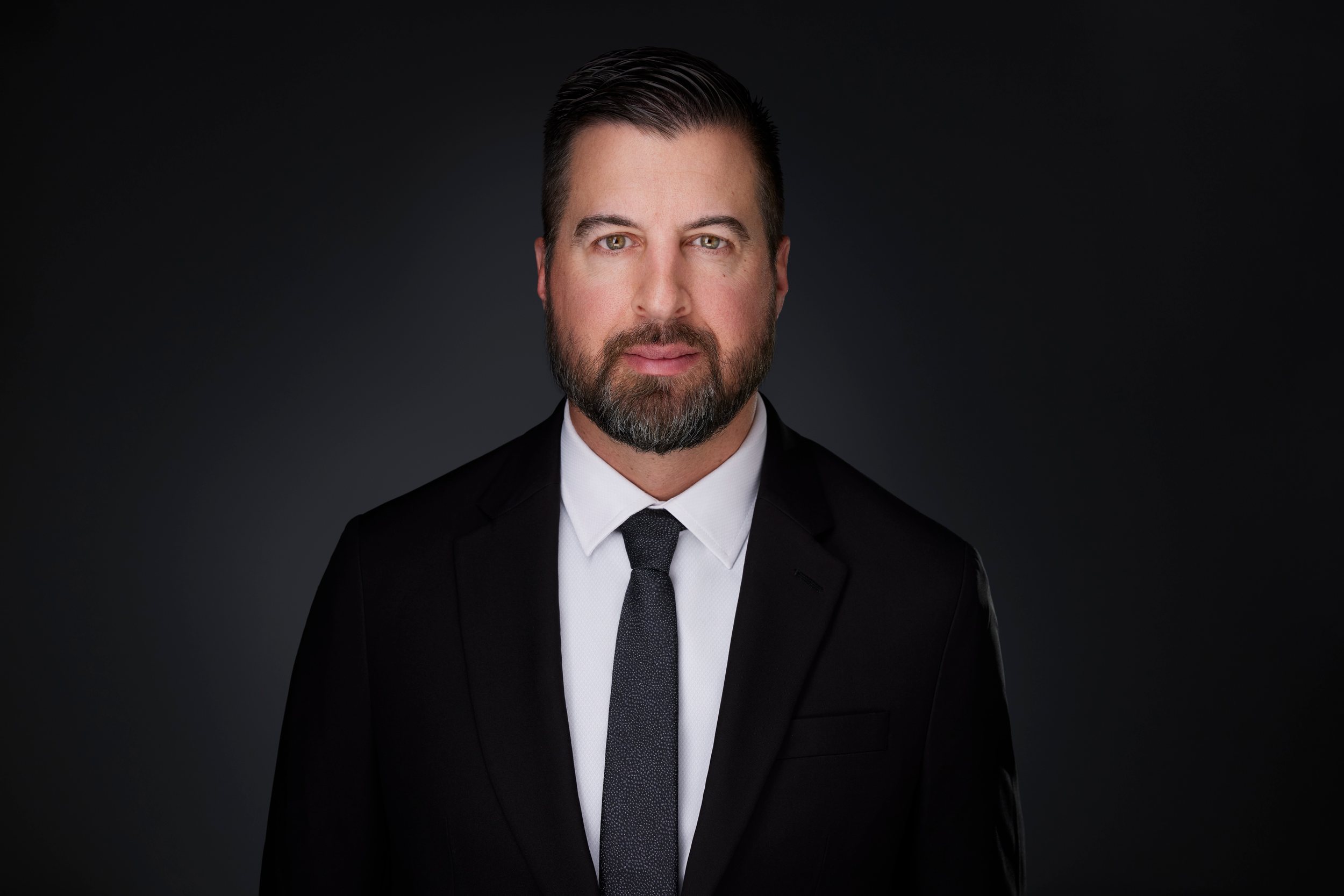 Real estate headshot: a beard, a black suit and a dark tie, on dark