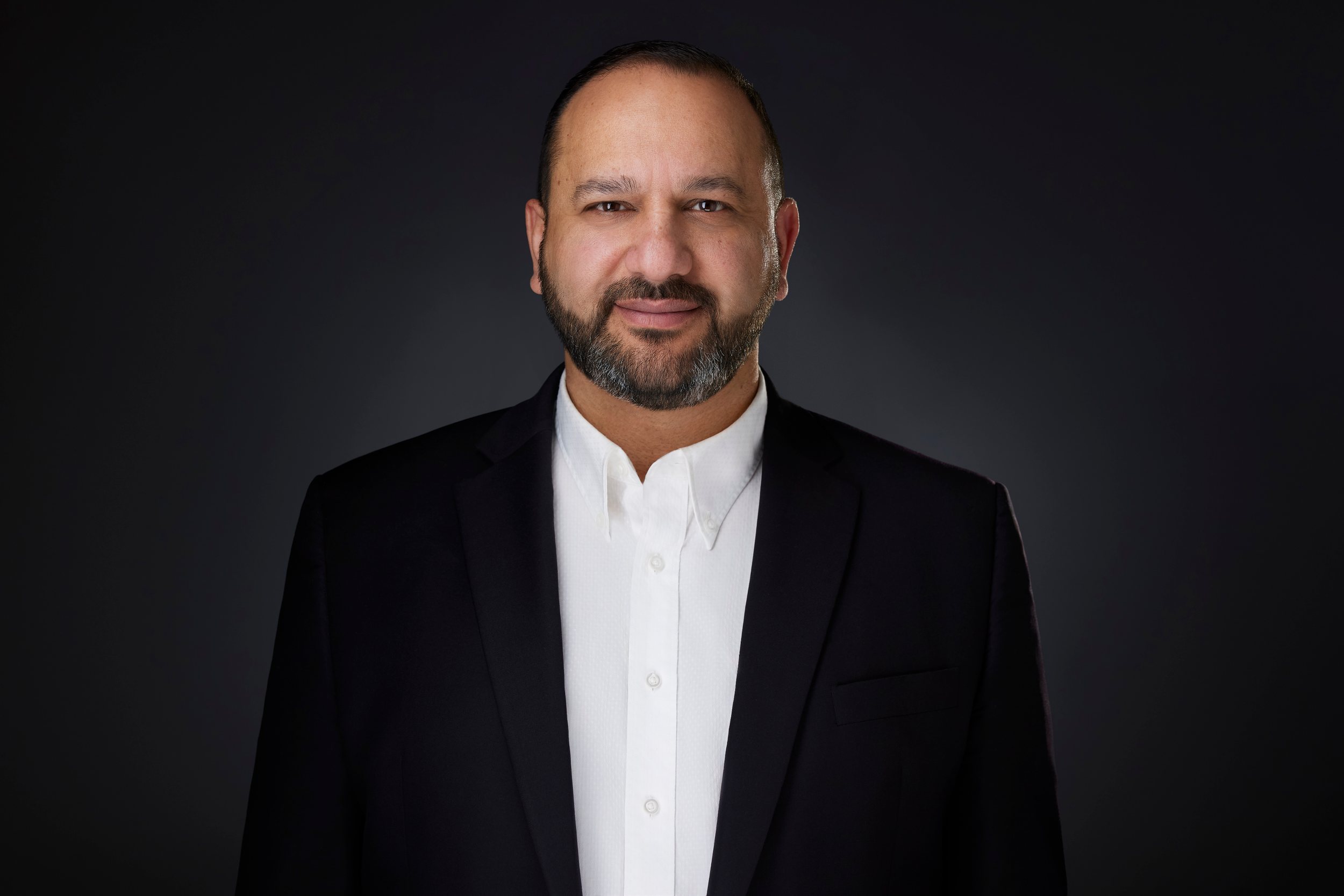 Real estate headshot: a beard, a black suit and an open white collar, on dark