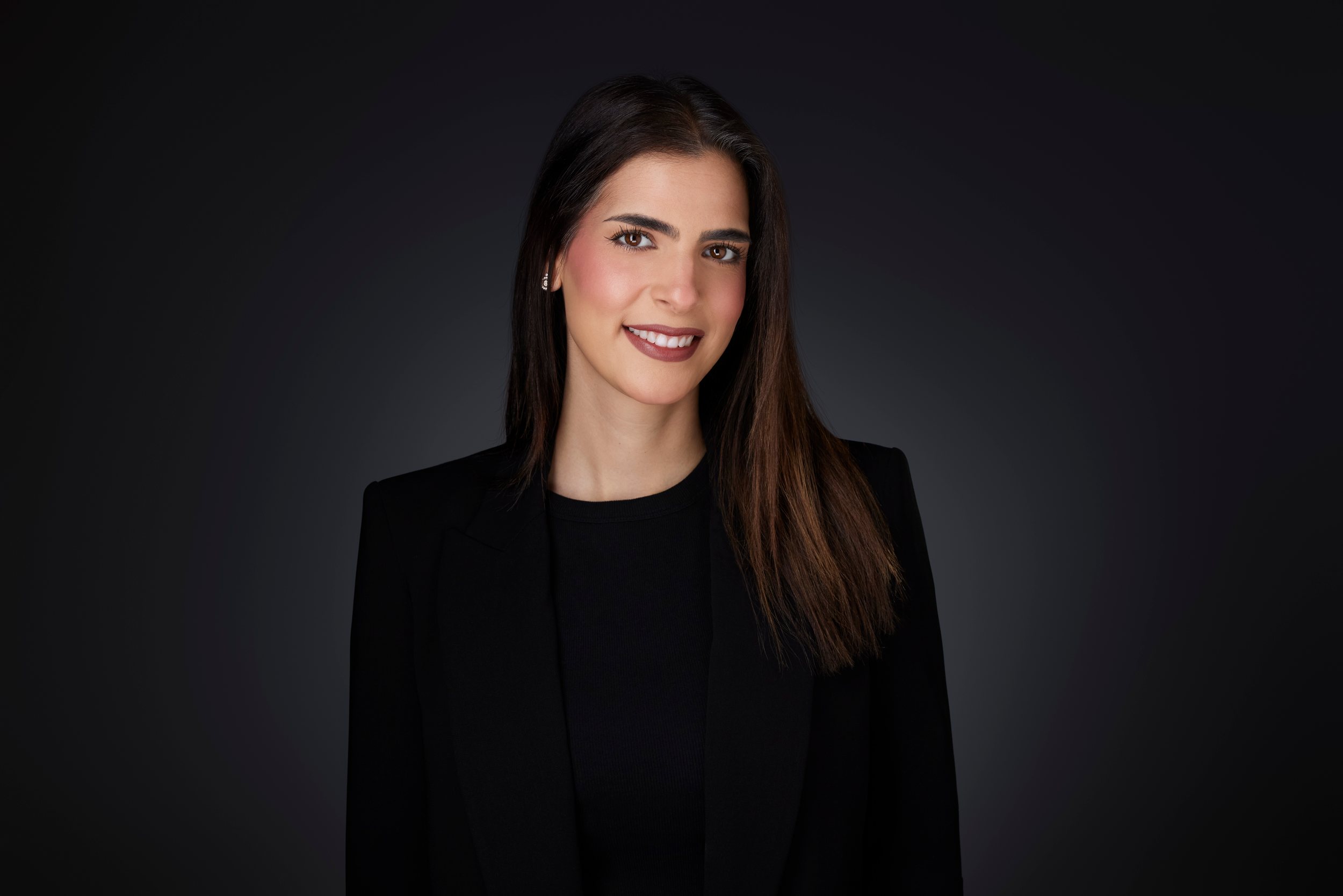 Real estate headshot: long dark hair, a black blazer over black, on dark