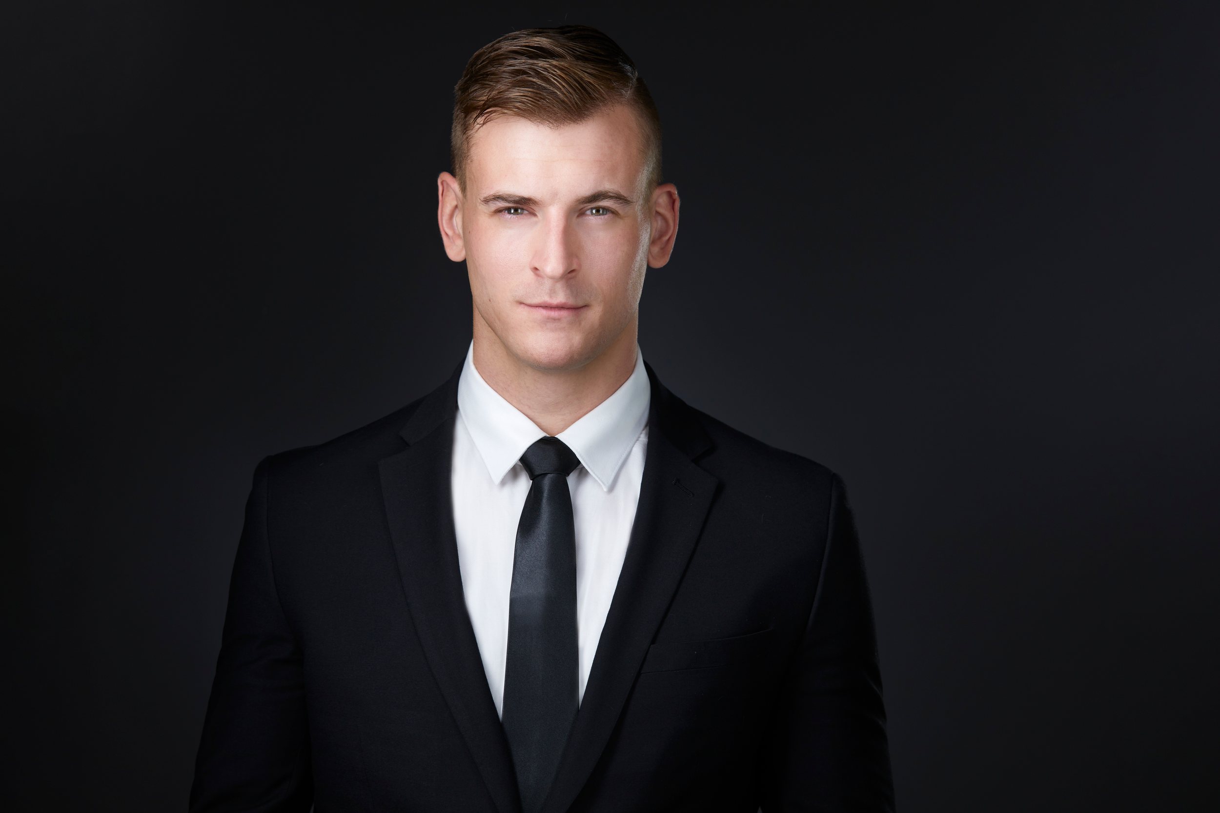 Real estate headshot: a black suit and a slim black tie, on dark